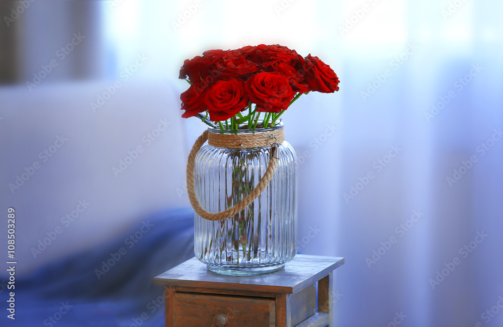 Red roses in a glass jar in the room