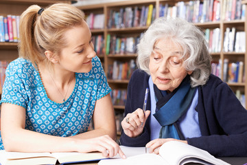 Senior Woman Working With Teacher In Library