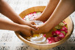 Closeup shot of a woman feet dipped in water with petals in a wooden bowl. Beautiful female feet at spa salon on pedicure procedure. Shallow depth of field with focus on feet.
