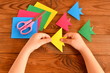 Origami colorful fish, paper sheets, scissors. Child holds an yellow origami fish in his hands. Brown wooden background 