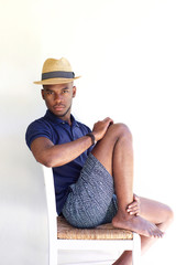 Wall Mural - Young african guy with hat sitting on a chair