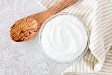 Wall Mural - Greek yogurt in a bowl, downward view with cloth and spoon on a white marble