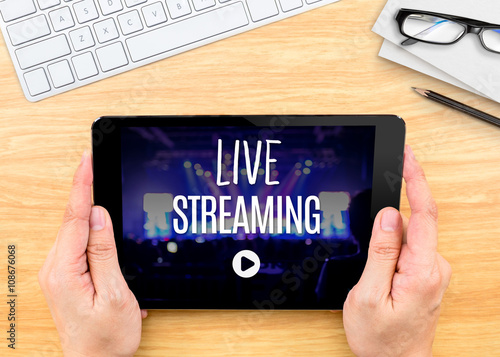Fotografie, Obraz Hand holding tablet with Live Streaming word on wood table ,Inte