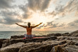 Young woman practices yoga on the rocks against the sea

