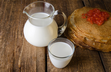 Wall Mural - Glass jug and glass with milk on a wooden rustic background. Traditional Russian pancakes with red caviar. Maslenitsa.