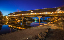 Frankenmuth Covered Bridge At Night. Frankenmuth Wooden Bridge Illuminated At Night With The City Skyline In The Background. Frankenmuth, Michigan.