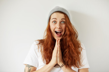 Wall Mural - Close up isolated portrait of young female with long loose red hair looking in excitement at the camera. Headshot of excited girl in white T-shirt and gray cap. Human face expressions. Film effect