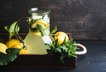 Homemade mint lemonade served with fresh lemons and ice over wooden background, top view, copy space