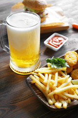 Wall Mural - Glass mug of light beer with French fries on dark wooden table, close up