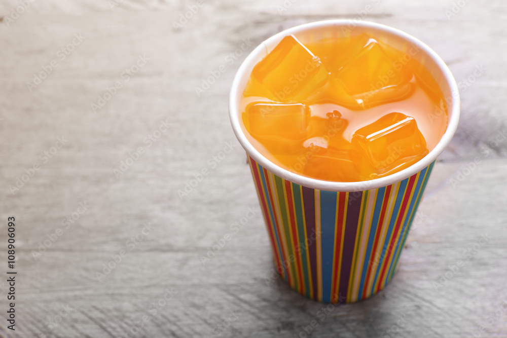 Orange drink in bright paper cup on wooden background