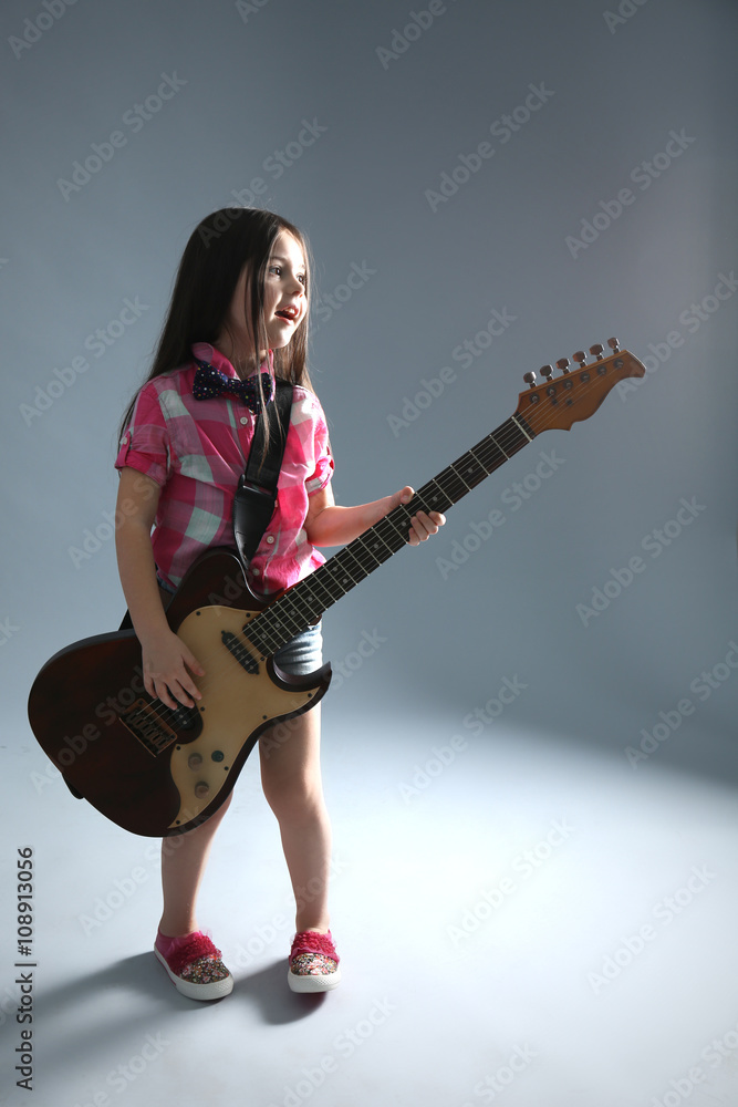 Beautiful artistic little girl playing guitar on grey background
