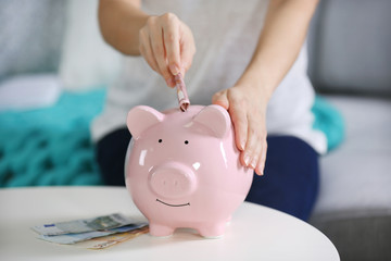 Poster - Female hand putting money into piggy bank closeup