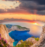 Fototapeta Morze - Navagio beach with shipwreck and flowers against sunset on Zakyn