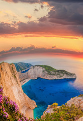 Fototapete - Navagio beach with shipwreck and flowers against sunset on Zakyn