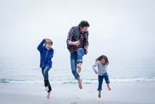 Cheerful Family Jumping At Sea Shore Against Clear Sky