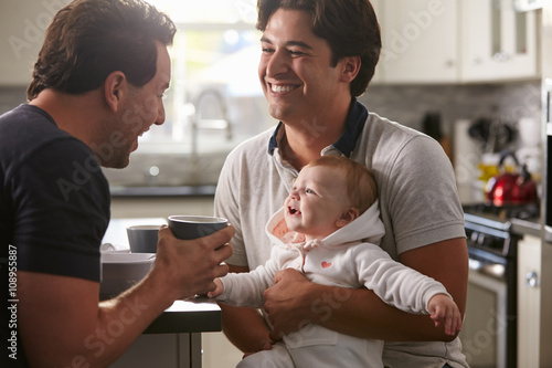 Fényképezés  Male gay couple holding baby girl in their kitchen