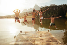 Young friends jumping into lake from a jetty