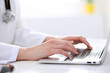© rogerphoto - Close-up of female doctor typing laptop sitting at a table in the hospital