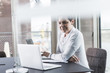 © Westend61 - Smiling businesswoman at desk looking at laptop