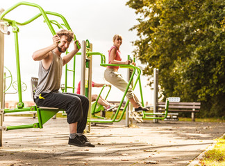 Active man and woman exercising at outdoor gym.