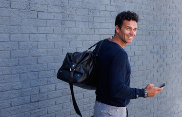 Wall Mural - Man turning around smiling with bag and mobile phone