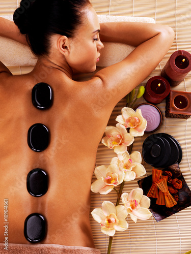 Fototapeta na wymiar Adult woman relaxing in spa salon with hot stones on body