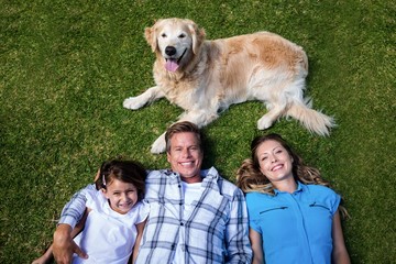 Wall Mural - Happy family lying ion grass with their dog