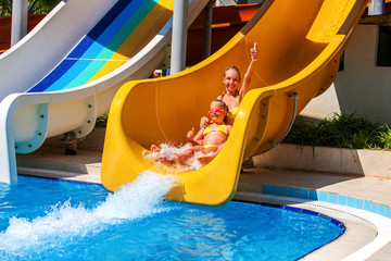 Wall Mural - Two children on water slide at aquapark and thumb up. Summer holiday. There are two water slides in aqua park. Outdoor.