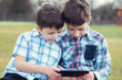 © sakkmesterke - Little boys playing on tablet in nature