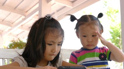 Wall Mural - Little Asian girls watching cartoon on cell phone together at home