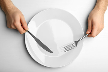 Male hands holding silver cutlery over plate, isolated on white