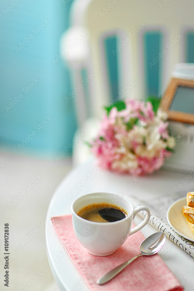 Cup of coffee with cookies on white table in light interior