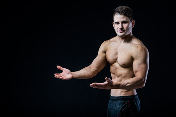 Wall Mural - Shirtless muscular athletic man point with two hands to blank copyspace. Sexy bodybuilder showing his body on black isolated background copy space.