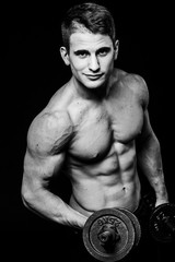 Wall Mural - Dark black and white contrast shot of young muscular fitness man stomach arm. Working out with dumbbells isolated