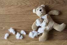 An Old, Sad Teddy Bear With His Stuffing Pulled Out And Scattered Over A Wooden Floor.