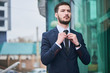 © amixstudio - The guy in the suit straightens his tie against the building with a glass facade