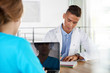 © AYAimages - Team of doctor and nurse discussing a patient diagnosis sitting at the desk in bright modern office