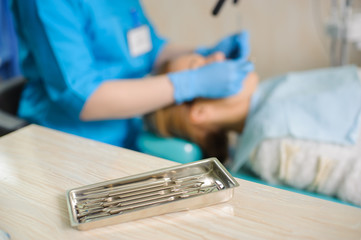 Wall Mural - Dentistry tools on foreground and dentist treating caries female patient's teeth on the background. Medical equipment. Oral procedure concept.