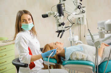 Wall Mural - Portrait of beautiful female dentist treating caries using microscope at the hospital, dentist smiling and looking at the camera. Dental care and treatment.