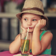 Melancholiac thinking kid girl in hat sitting in cafe and drinki