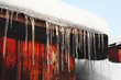 Icicle and snow on the roof. Cold season. Snowdrift and icicle on the roof of a  country wooden house in the winter. Blue sky background.