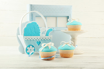 Wall Mural - Tasty cupcakes with bow and baby shoes, decorative baby carriage and photo album  on color background