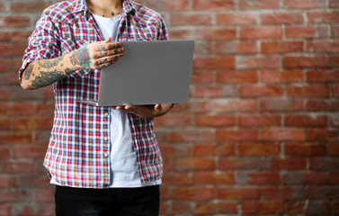 Poster - Young man with tattoo holding laptop on brick wall background