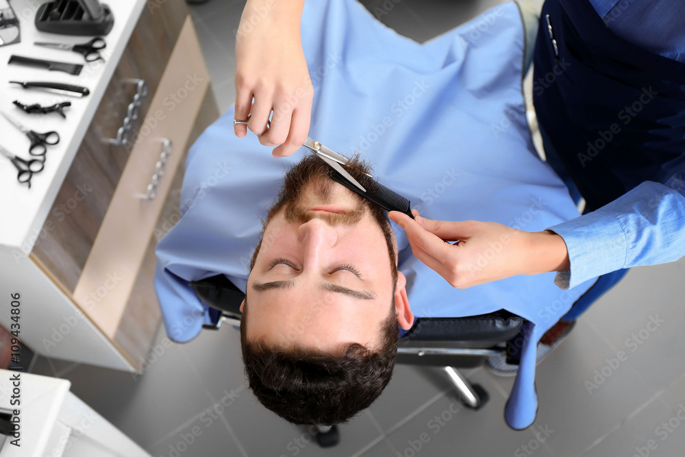 Professional hairdresser cutting beard with scissors
