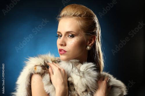 Young beautiful blonde girl wearing perfect makeup in a fur over dark ...
