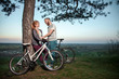 © mikhail_kayl - A young couple in love standing under a tree and hugging at sunset, standing next to the bike