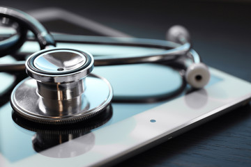 stethoscope and tablet on dark wooden background