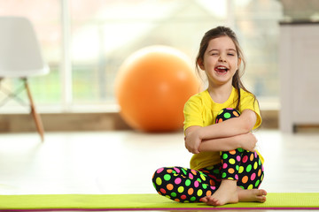 Little funny girl sitting on a mat indoor