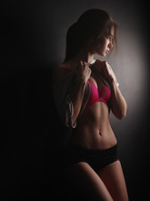 Thoughtful And Tempting Young Woman With Sexy Shape, Beautiful Press And Slim Gorgeous Body In The Bright Pink Underwear And Little Shorts Posing In The Studio On The Black Wall At The Background