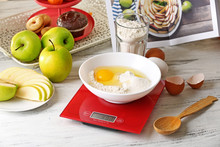 Bowl Of Raw Egg And Flour With Digital Kitchen Scales On Light Wooden Table